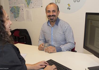 Een breed glimlachende man, zitten aan het bureau van een medewerker