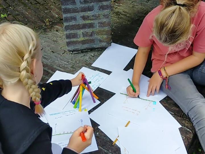 Twee kinderen drie met gekleurde stiften op witte vellen papier aan het tekenen zijn.