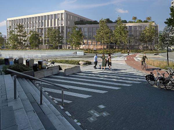 Op een zebrapad staan mensen die lopen richting een wit gebouw. Naast het zebrapad ligt een fietspad en een weg (rotonde). Voor het witte gebouw staan bomen en bovenop het dak van het gebouw staan planten.